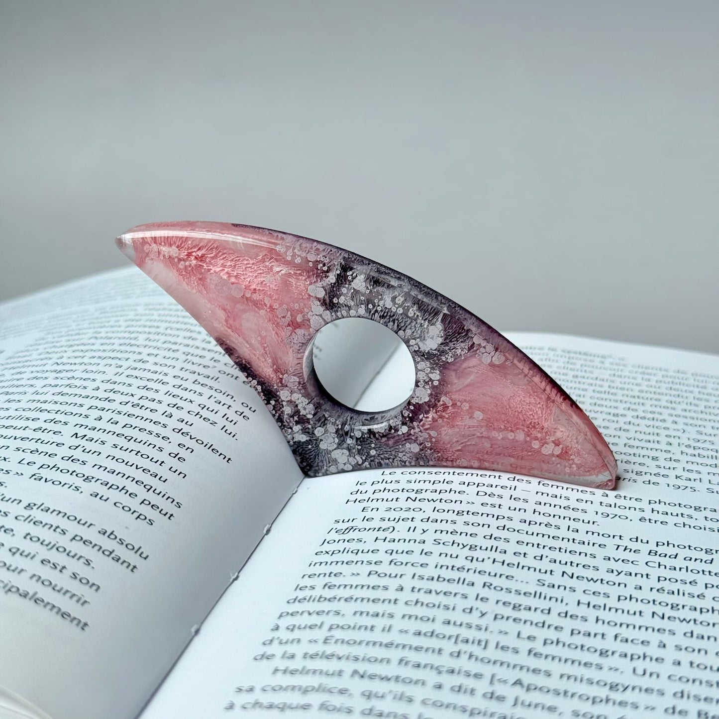 Curved pink and gray resin page holder with petri ink design placed in an open book.