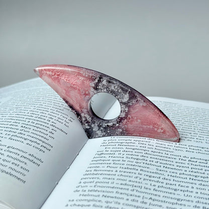 Curved pink and gray resin page holder with petri ink design placed in an open book.